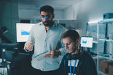 Two men in an office collaborate while examining a computer screen together.